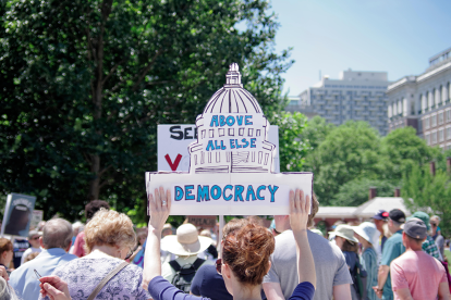 Woman holding a sign that reads "Above all else Democracy"
