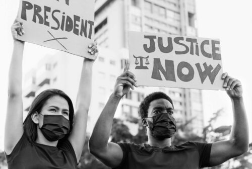 Photo of two people with arms raised holding protest signs