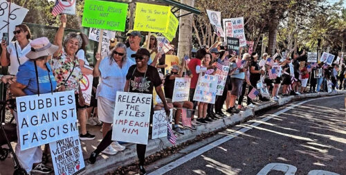Protesters holding signs standing on a sidewalk.